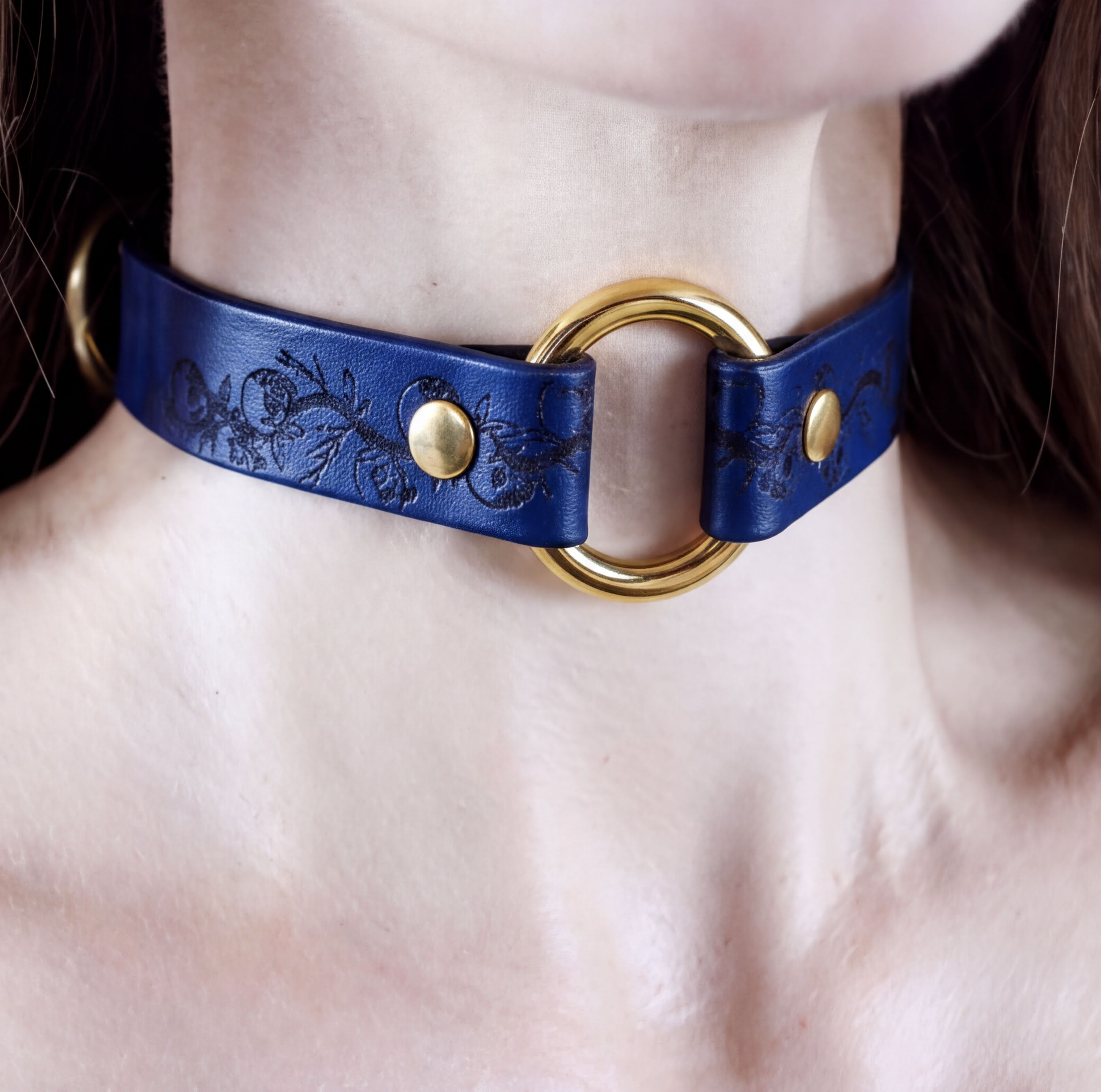 A close-up view of a woman's neck and chest area wearing a blue choker necklace with a gold ring.