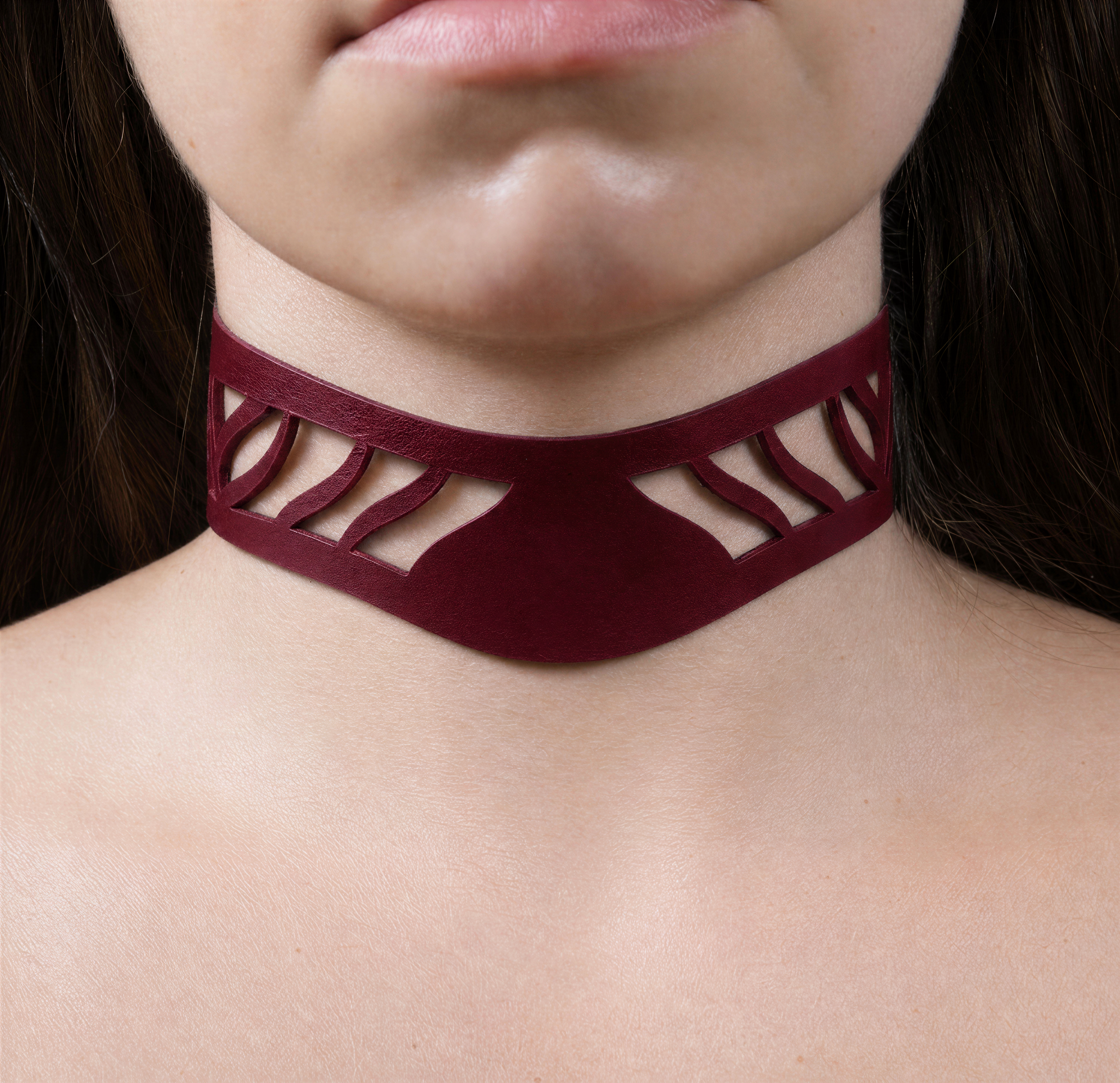 A close-up of a person's neck and chest area wearing a burgundy choker necklace with a unique cutout design.