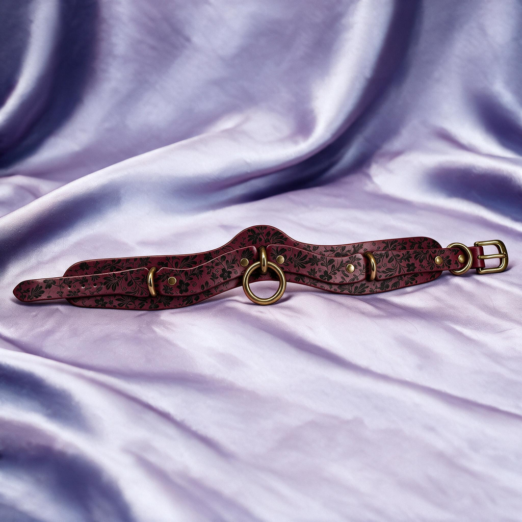 A burgundy leather choker necklace with a floral pattern and metal rings is displayed on a purple satin background.