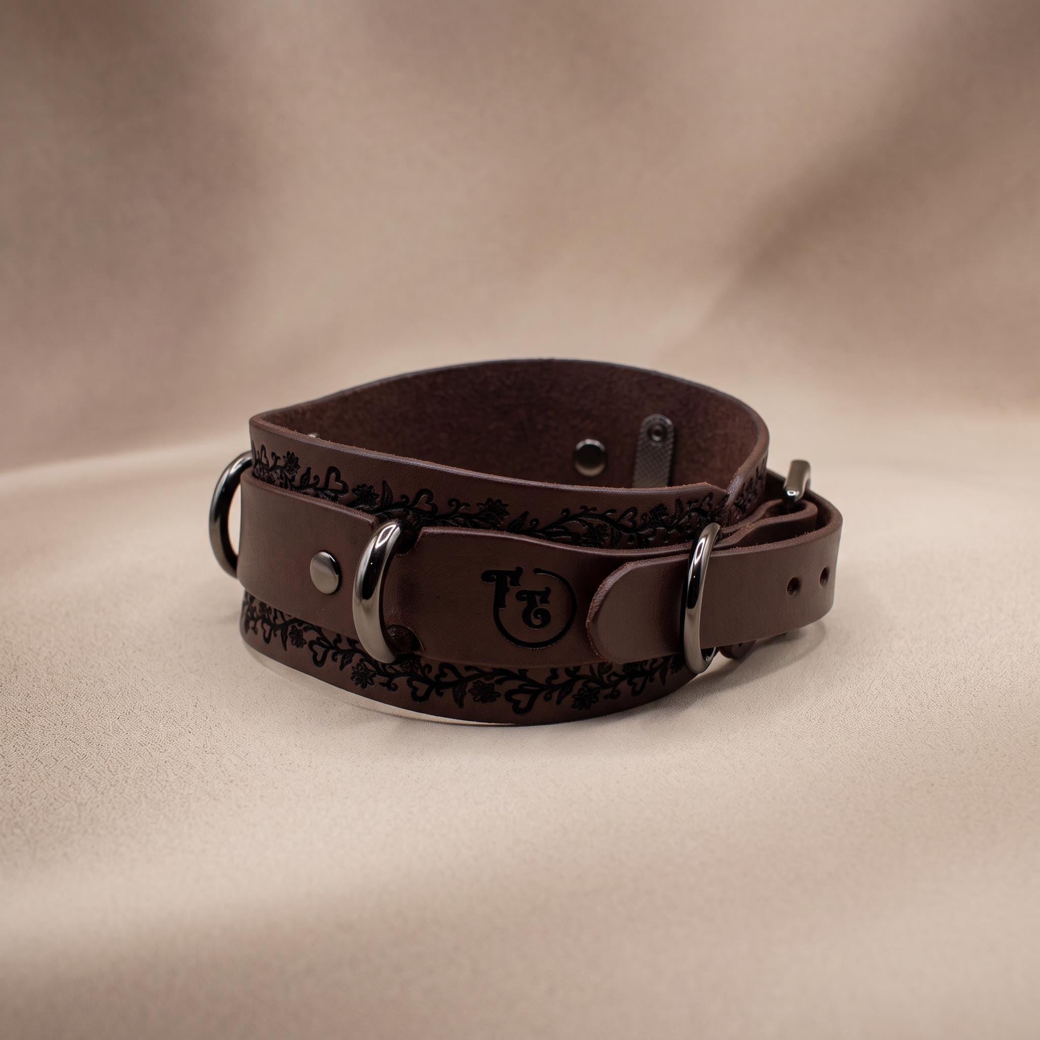 A brown leather choker collar with metal buckles and a decorative pattern on the surface.