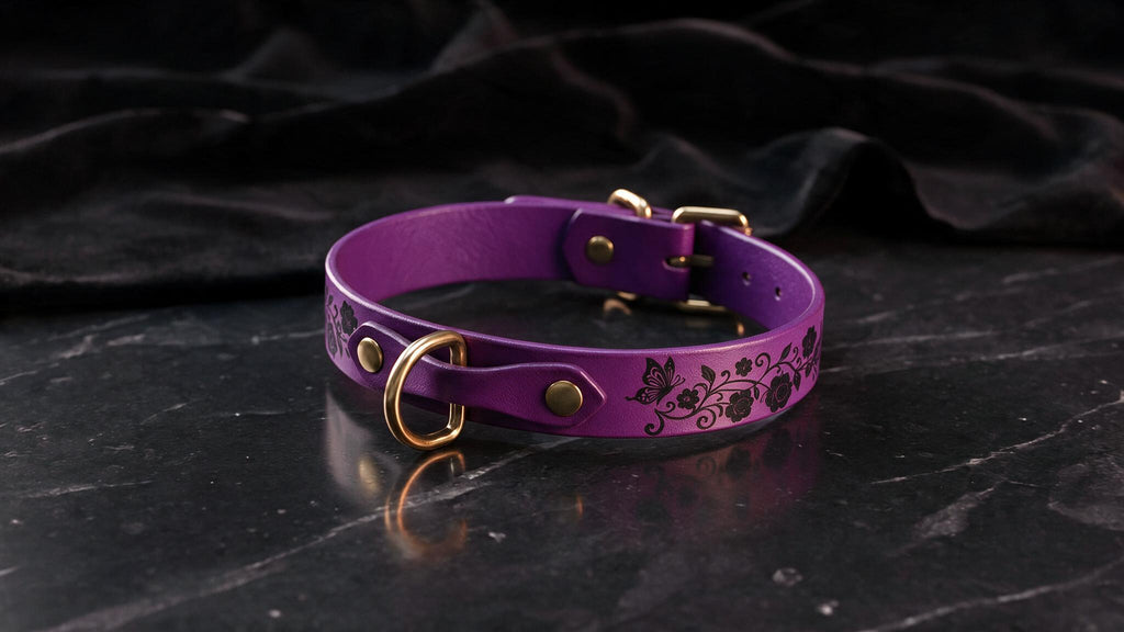 A purple leather collar with a floral design and gold hardware is displayed on a black marble surface.