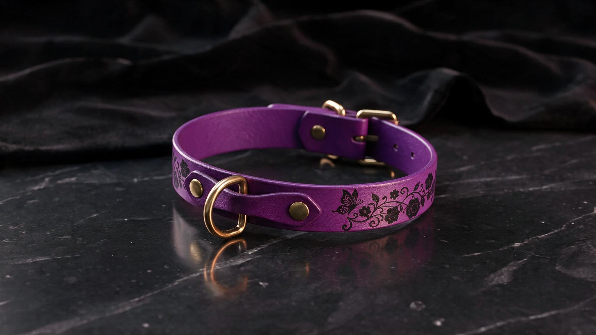 A purple leather collar with a floral design and gold hardware is displayed on a black marble surface.