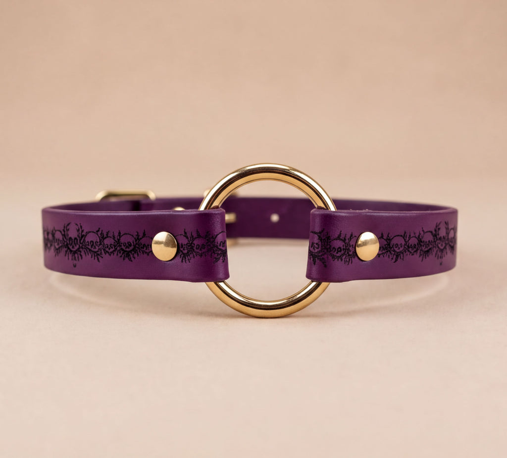 A purple leather choker collar with a gold-colored circular buckle.