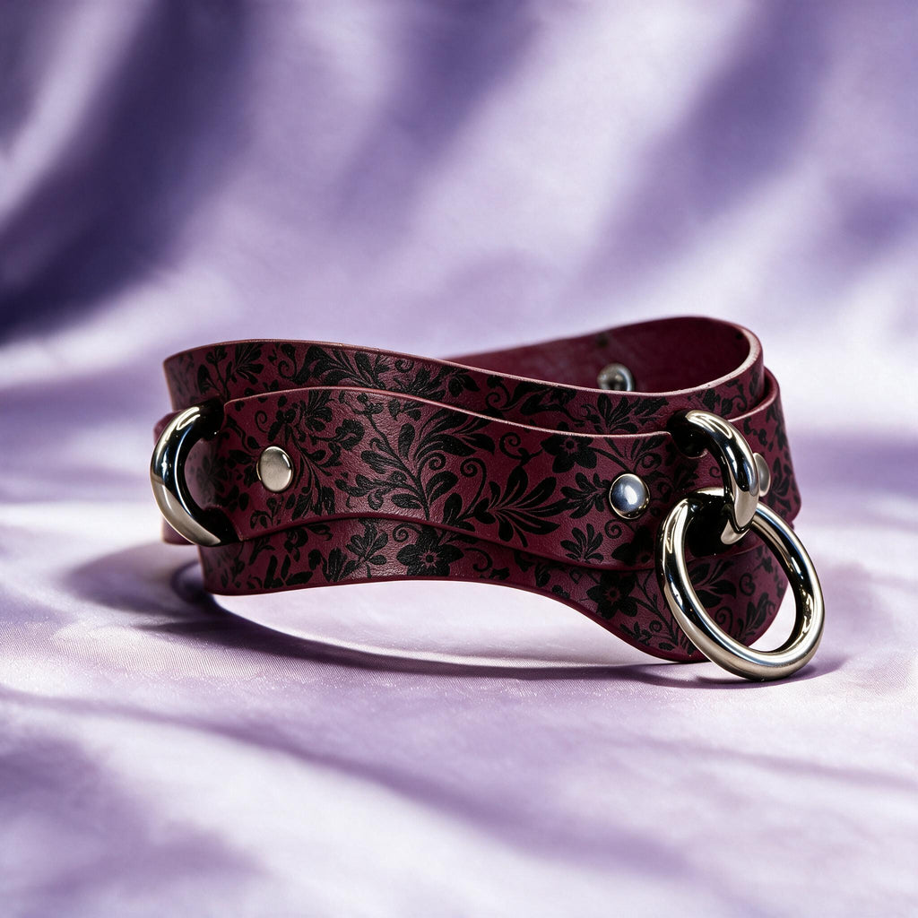 A burgundy leather choker with a floral pattern and metal rings is displayed against a purple background.