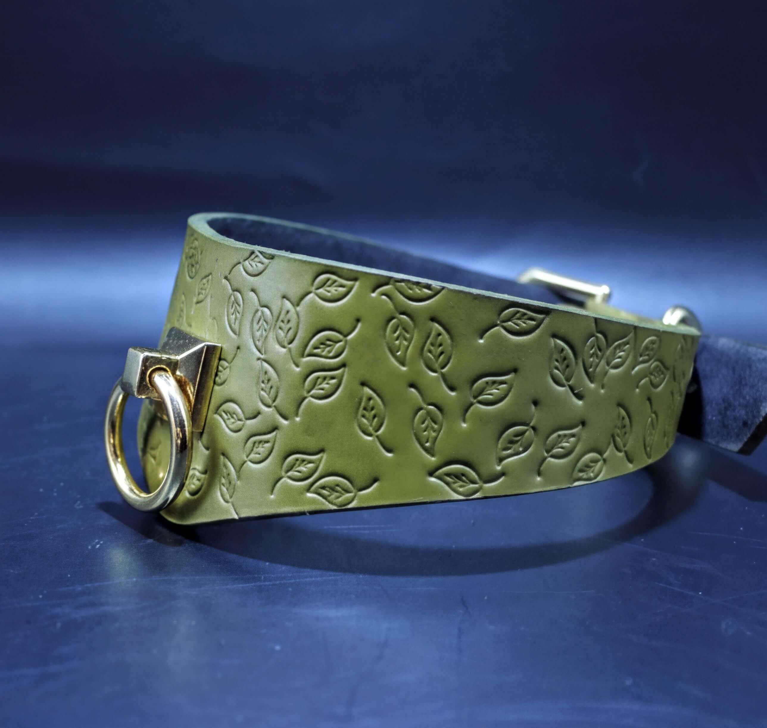 A green leather collar with a leaf pattern embossed on it, featuring a gold-colored metal ring and buckle.