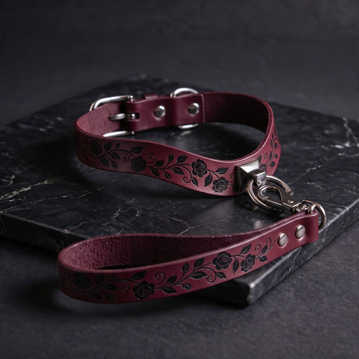 A burgundy leather collar with a floral pattern and a matching leash is displayed on a dark surface.