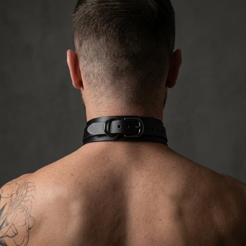 the back of a man's neck and shoulders, with a black leather choker collar around his neck.