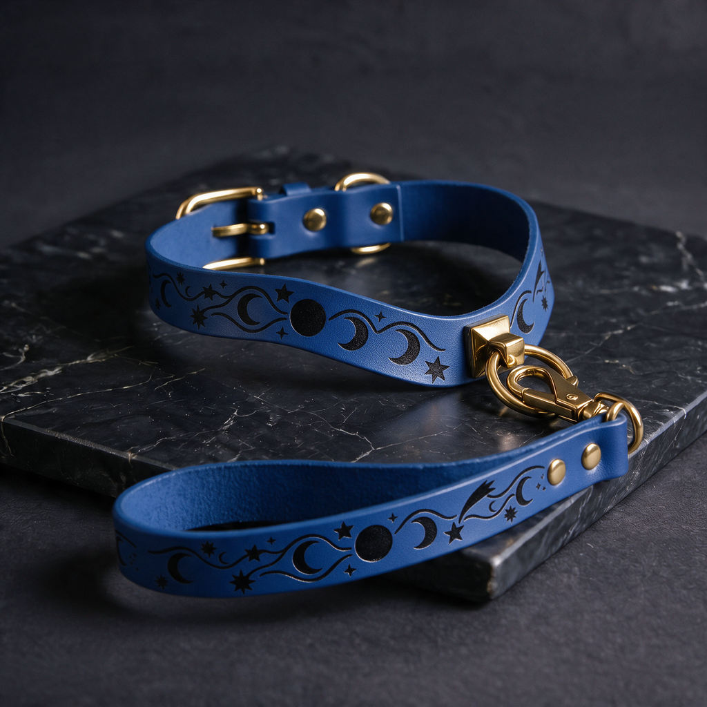 A blue leather dog collar with a star and moon design, featuring a gold buckle and a matching star-shaped tag, is displayed on a black marble surface.