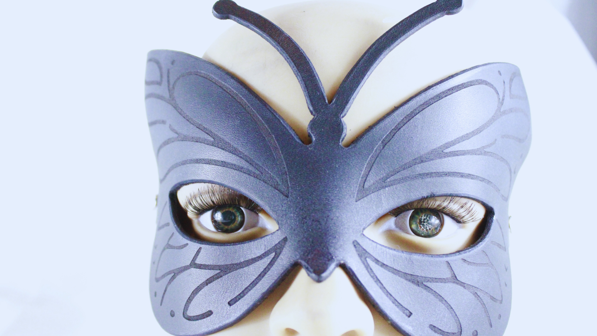 A close-up of a mannequin head wearing a butterfly-shaped mask with large eyes.