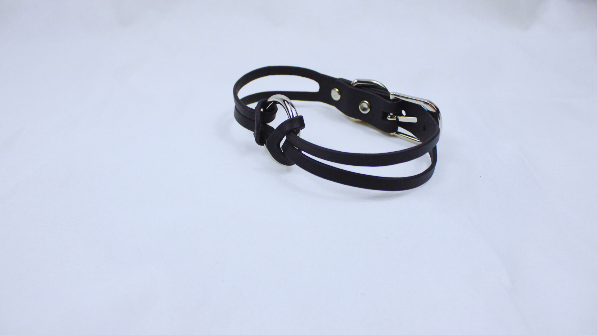 A black leather bracelet with a silver buckle is shown against a white background.