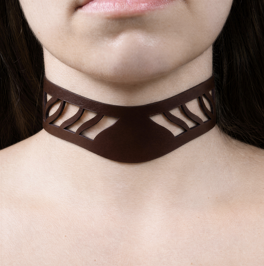 A close-up of a person's neck and chest area wearing a brown choker necklace with a unique cutout design.