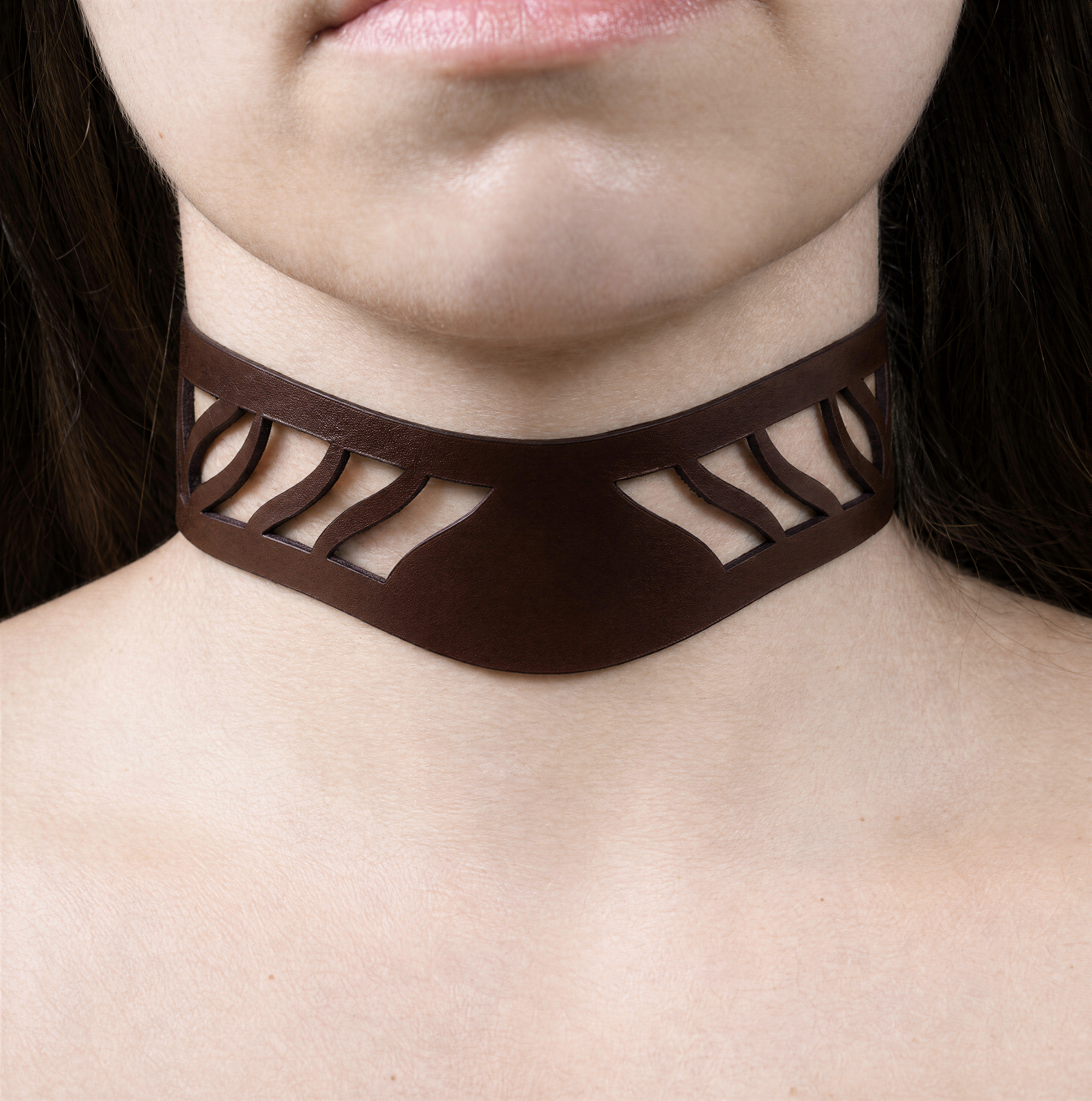 A close-up of a person's neck and chest area wearing a brown choker necklace with a unique cutout design.