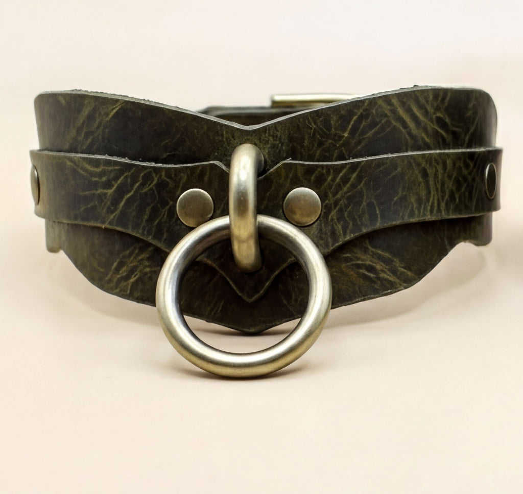 A close-up image of a leather choker necklace with a metal ring and buckle.