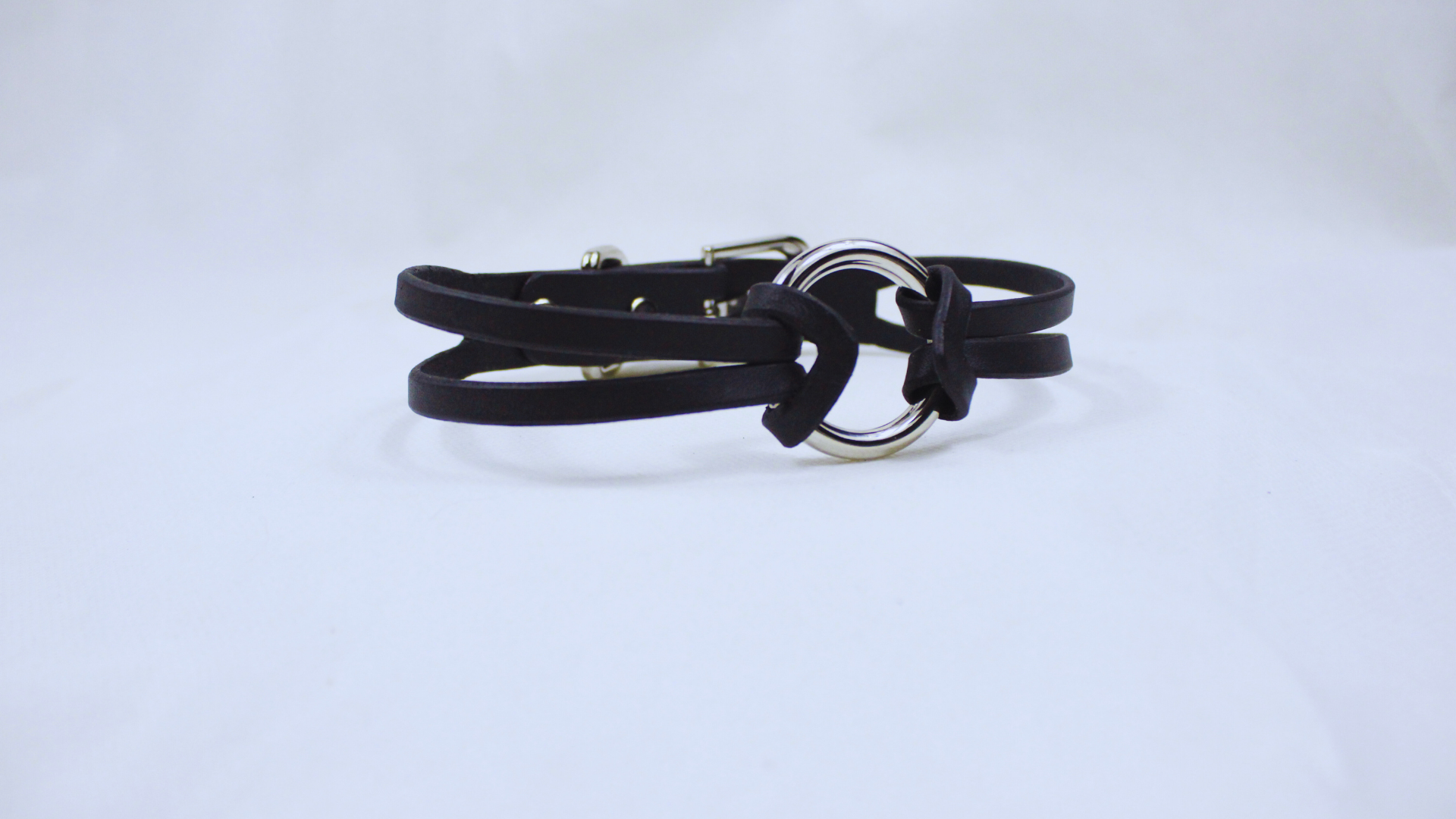 A black leather bracelet with a silver metal ring and buckle is shown against a white background.