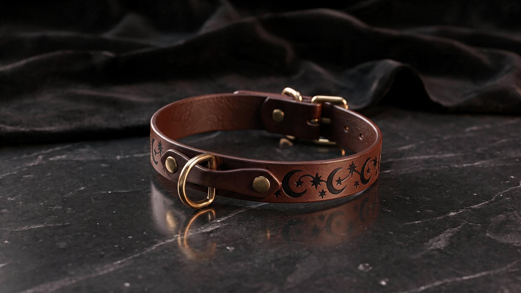 A brown leather collar with a moon and star design sits on a dark surface.