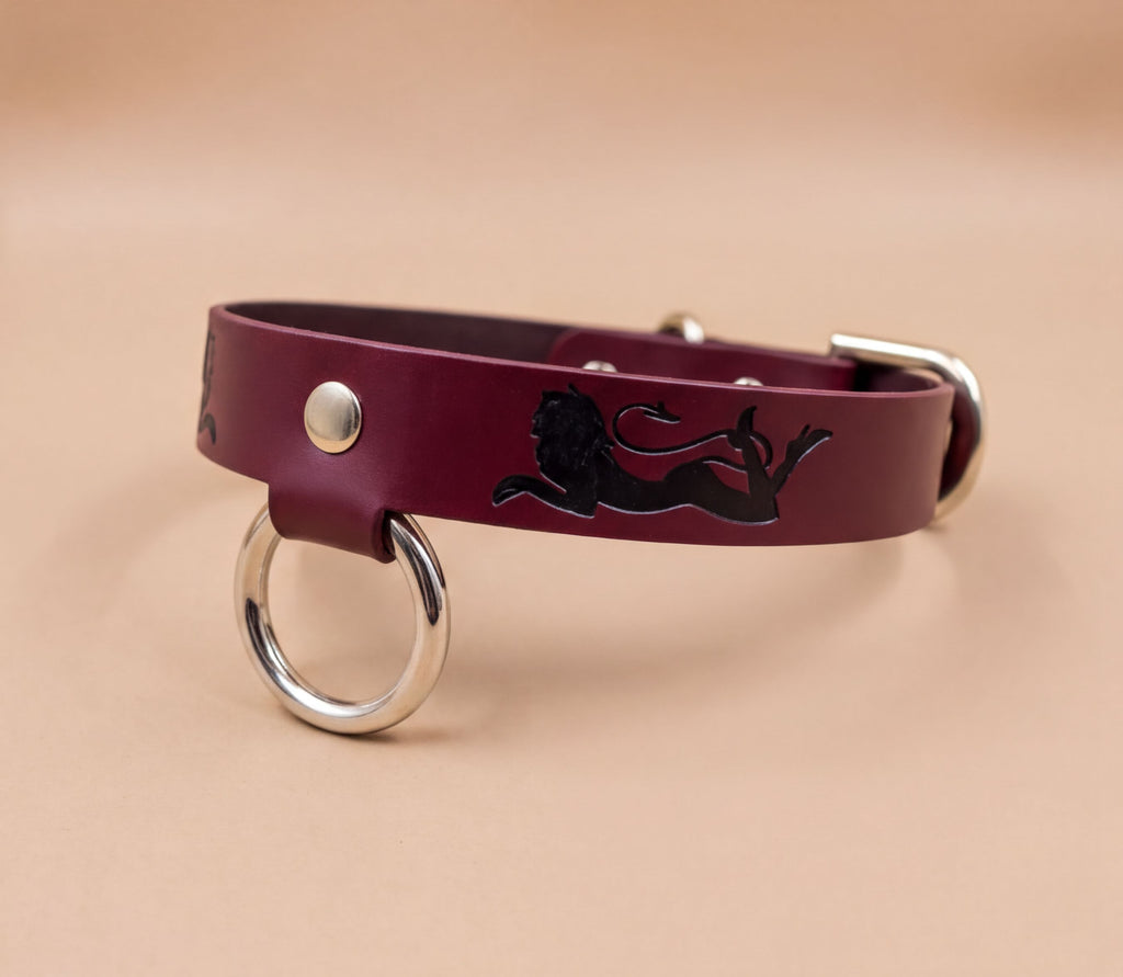A burgundy leather dog collar with a black lion design and metal ring.