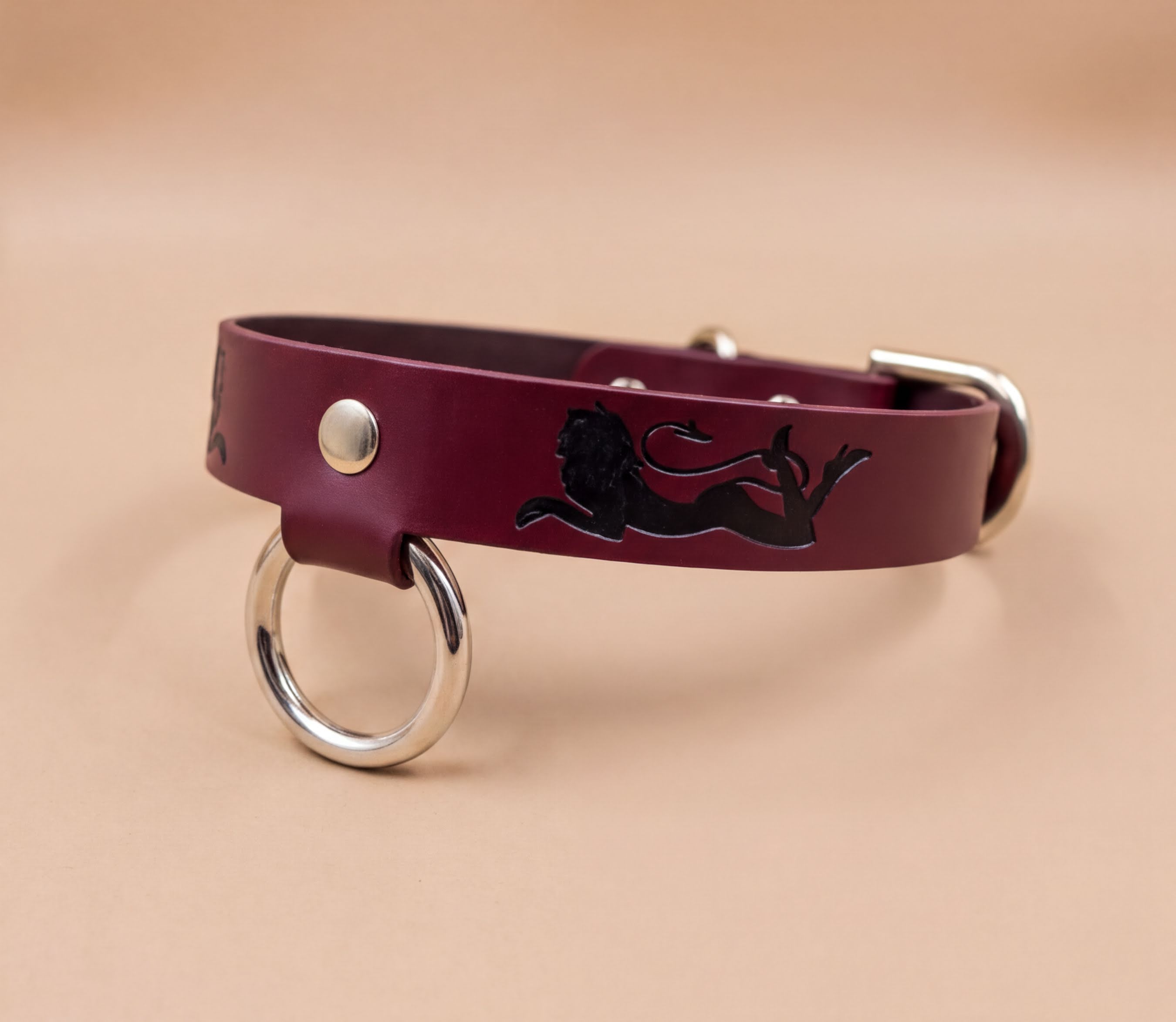 A burgundy leather dog collar with a black lion design and metal ring.