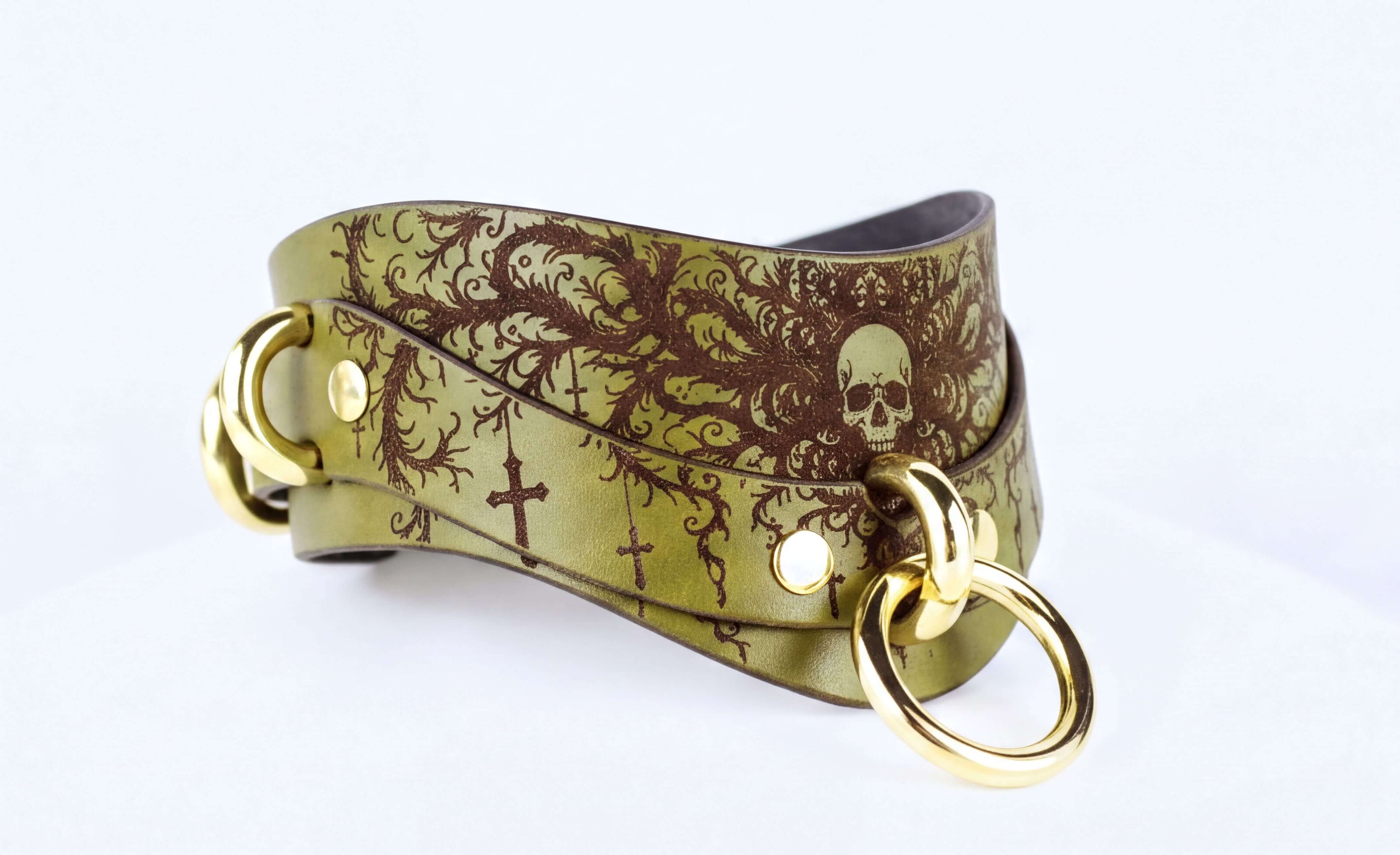 A gold-colored leather choker necklace with a skull design and floral patterns.