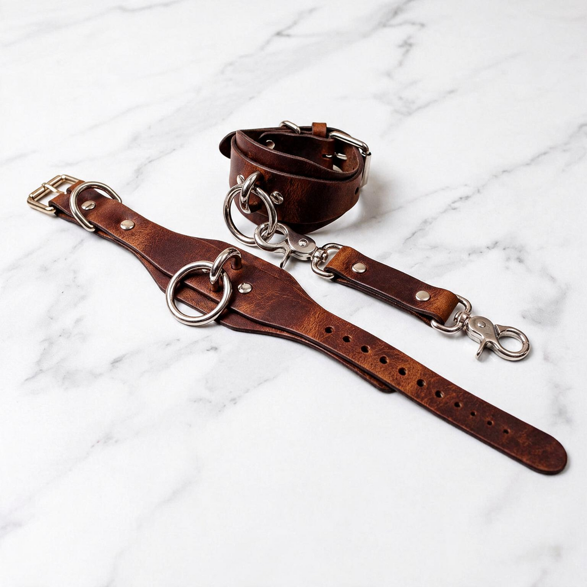 a pair of brown leather straps with metal rings and buckles, laid out on a marble surface.