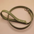 A green leash with a metal attachment is shown on a light-colored surface.