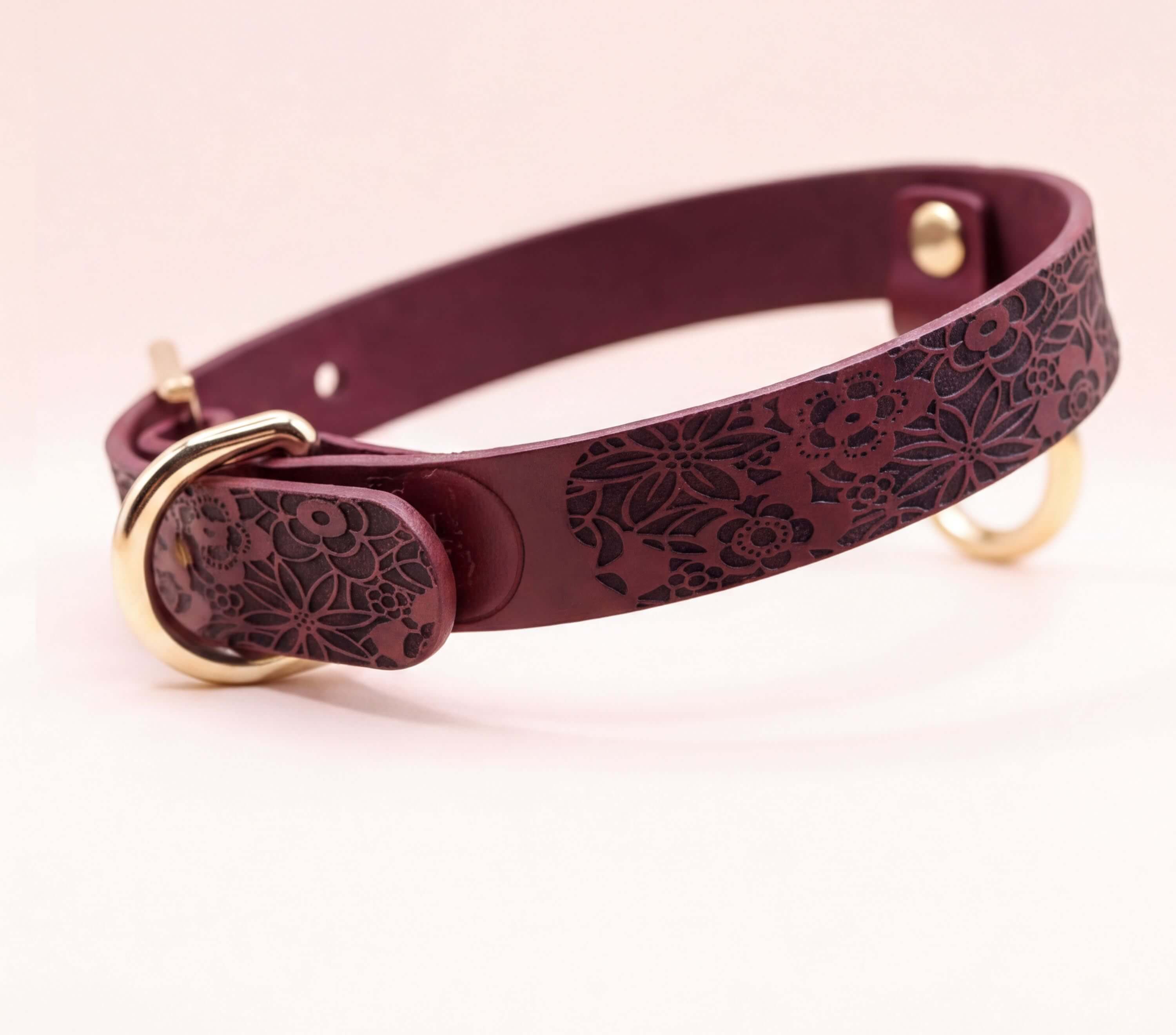 A burgundy leather collar with a floral pattern and a gold buckle.