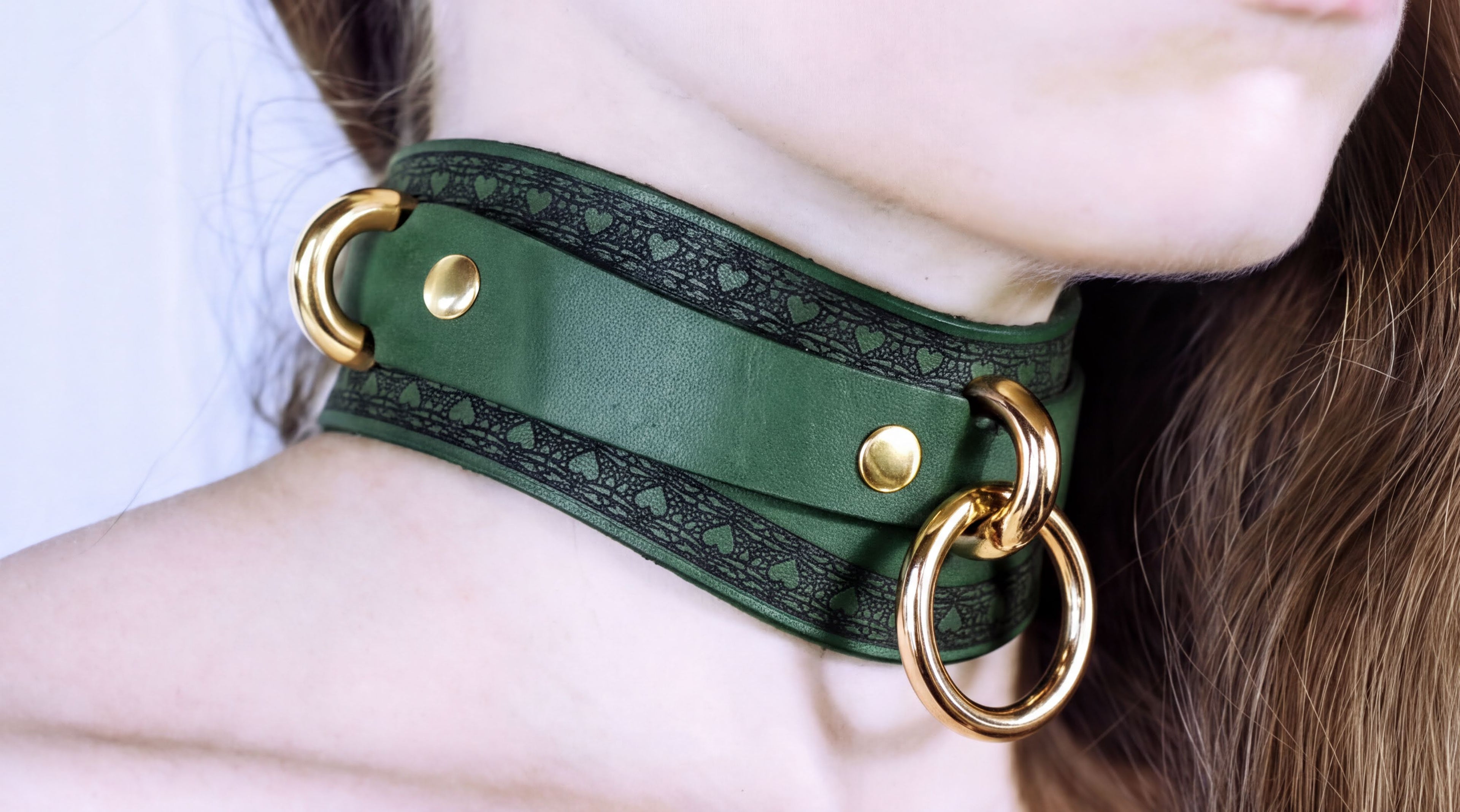 A close-up of a person's neck wearing a green leather choker with gold rings and a decorative pattern.