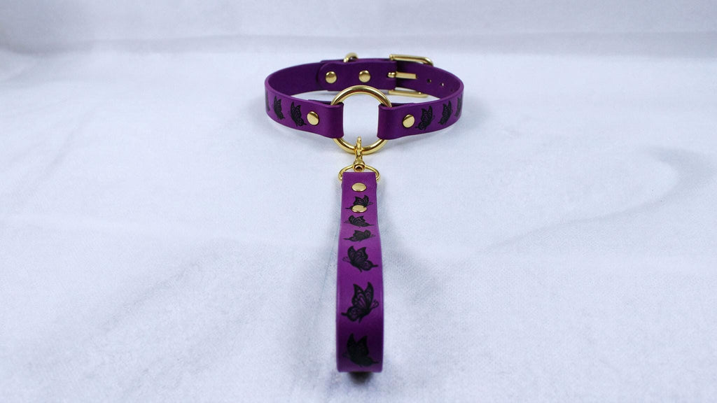 A purple collar with a gold buckle and a black cat design on it, placed on a white surface.