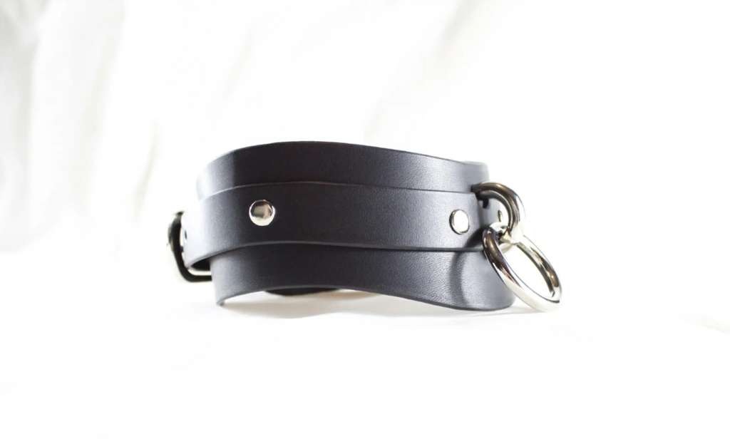A black leather choker necklace with metal rings and buckles.