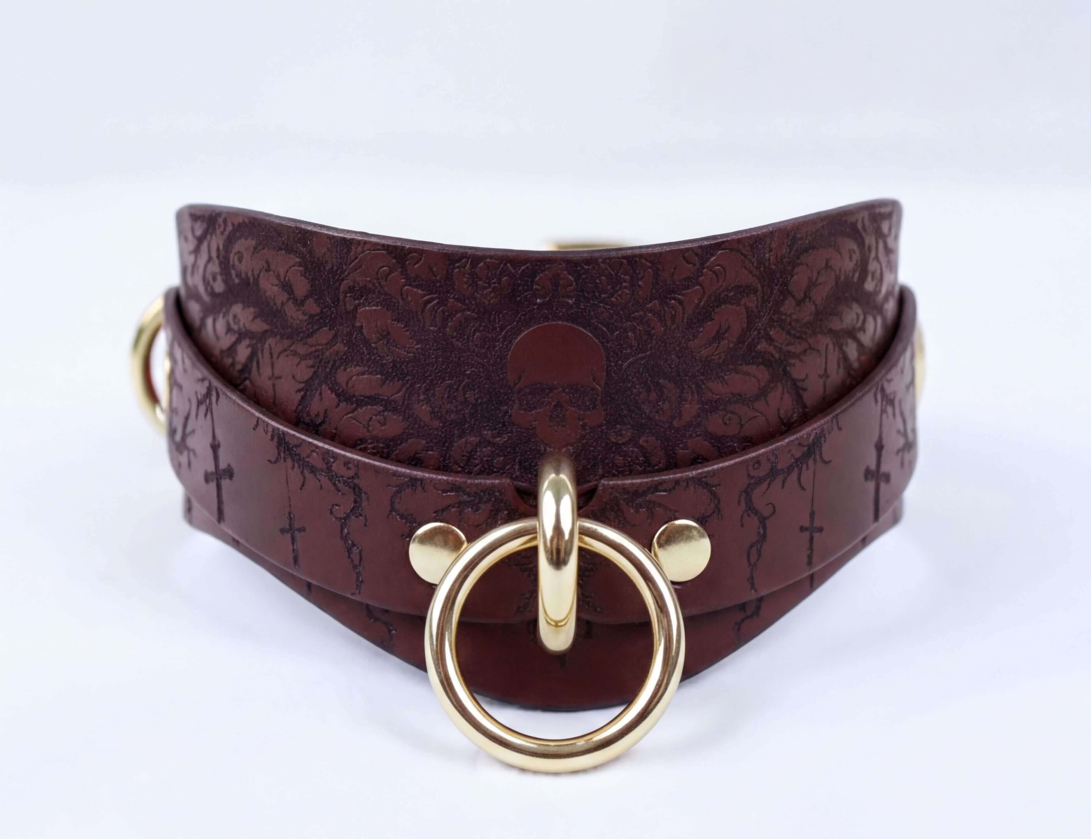 A brown leather choker necklace with a gold-colored metal ring and a skull design on the front.