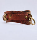 A brown leather strap with a metal ring and two brass buckles, featuring a distinctive tree-like pattern.