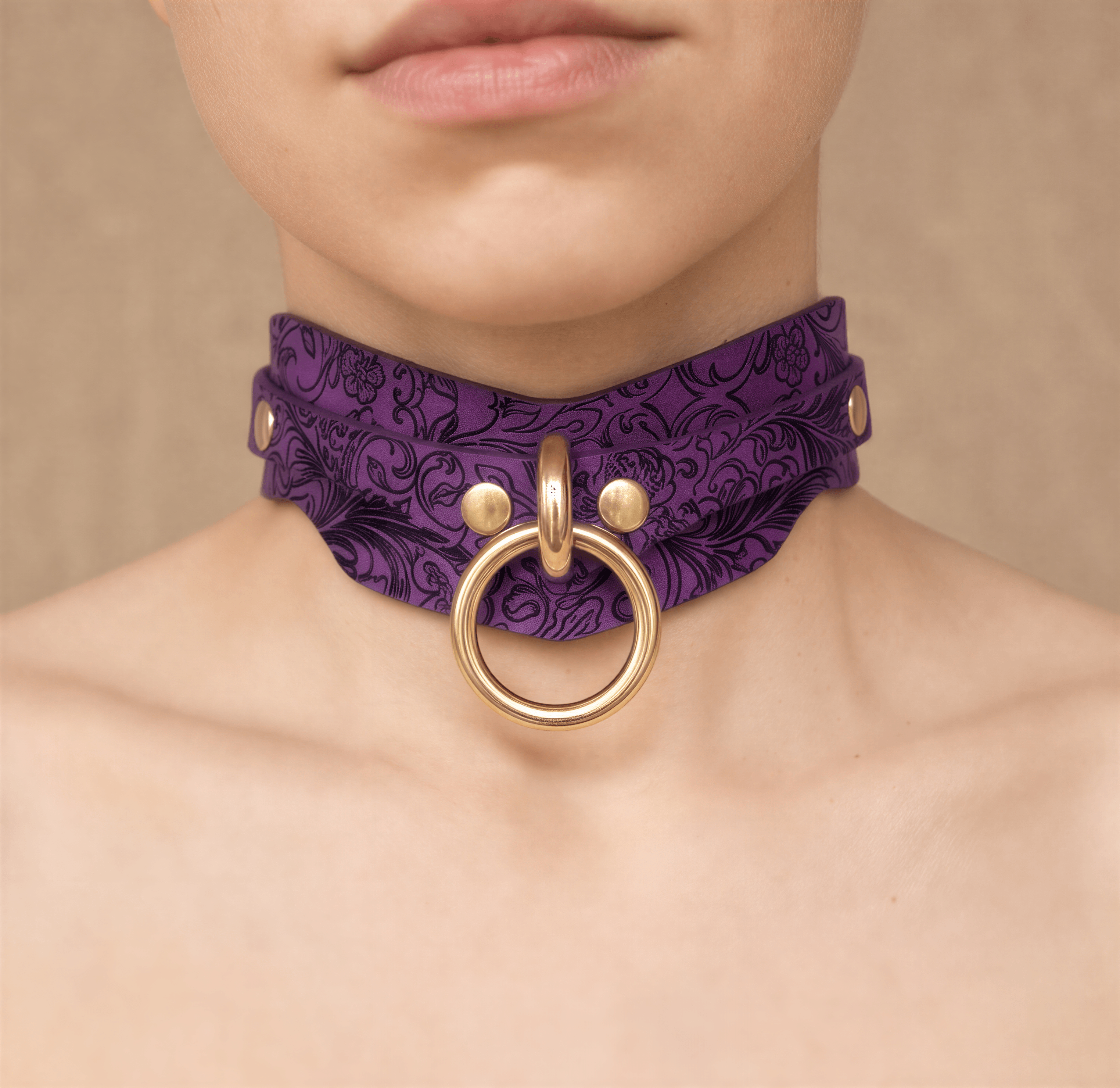A close-up of a person's neck wearing a purple choker necklace with a gold ring and buckle.
