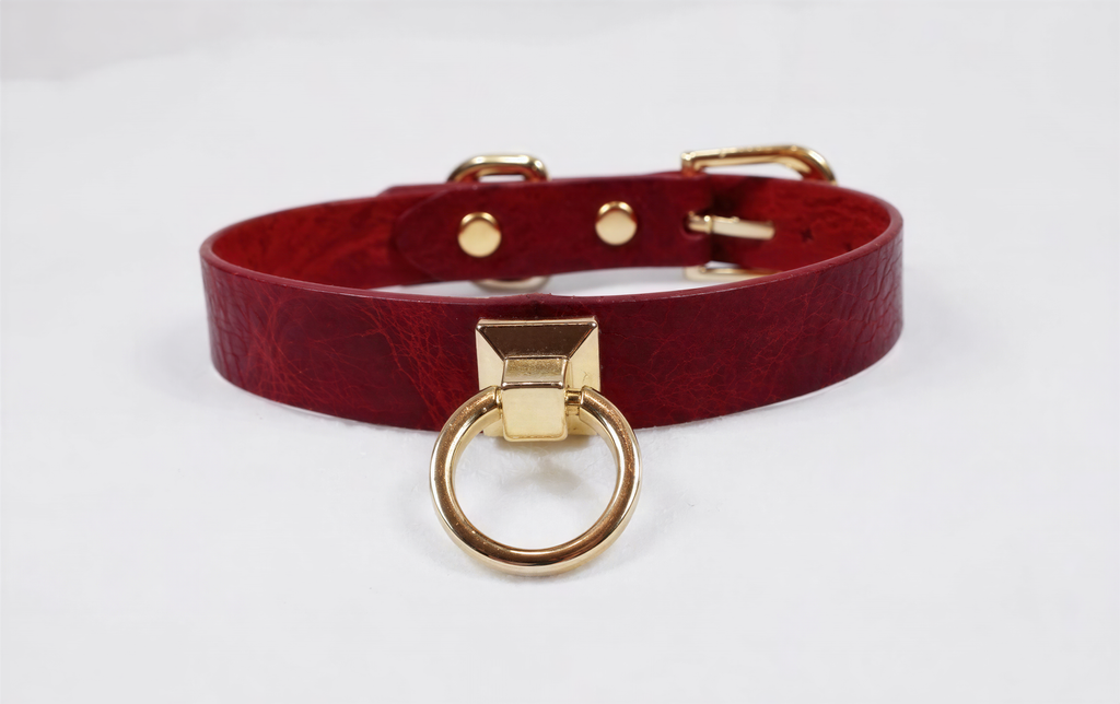 A red leather choker collar with a gold-colored metal ring and buckle.