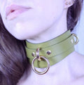 A close-up of a person's neck wearing a green leather choker necklace with gold-colored metal rings.