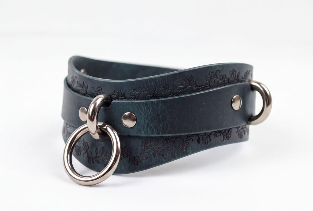 A dark green leather choker necklace with metal rings and a floral pattern on the surface.