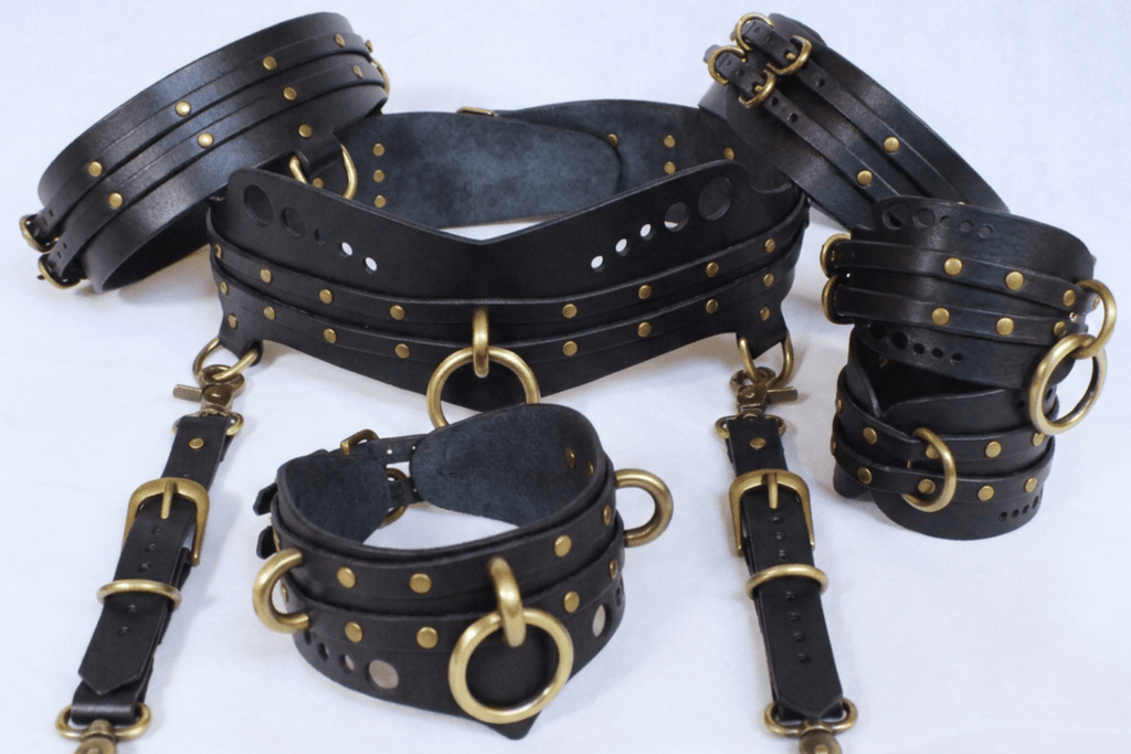 A collection of black leather straps with gold-colored buckles and rivets, arranged on a white background.