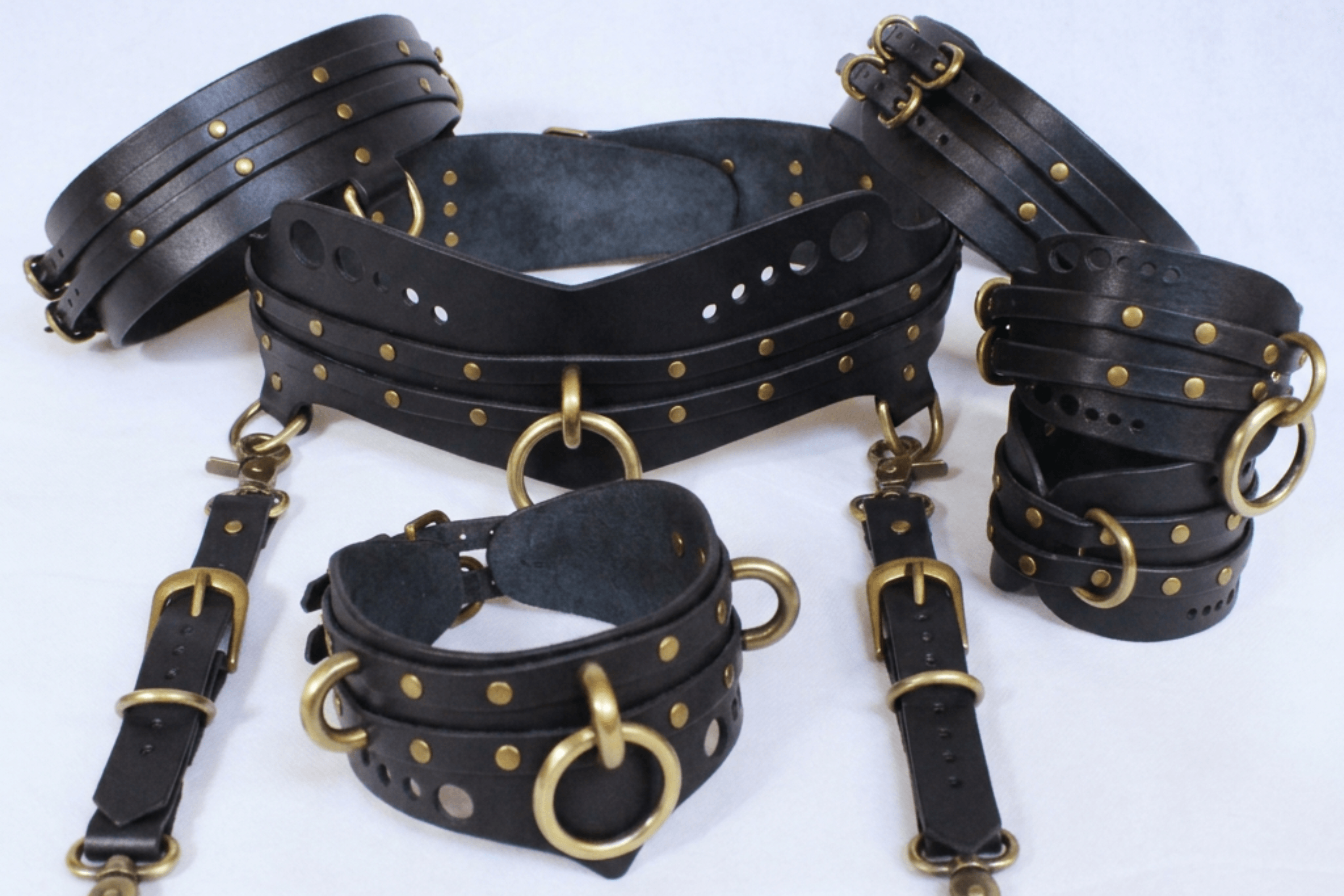 A collection of black leather straps with gold-colored buckles and rivets, arranged on a white background.