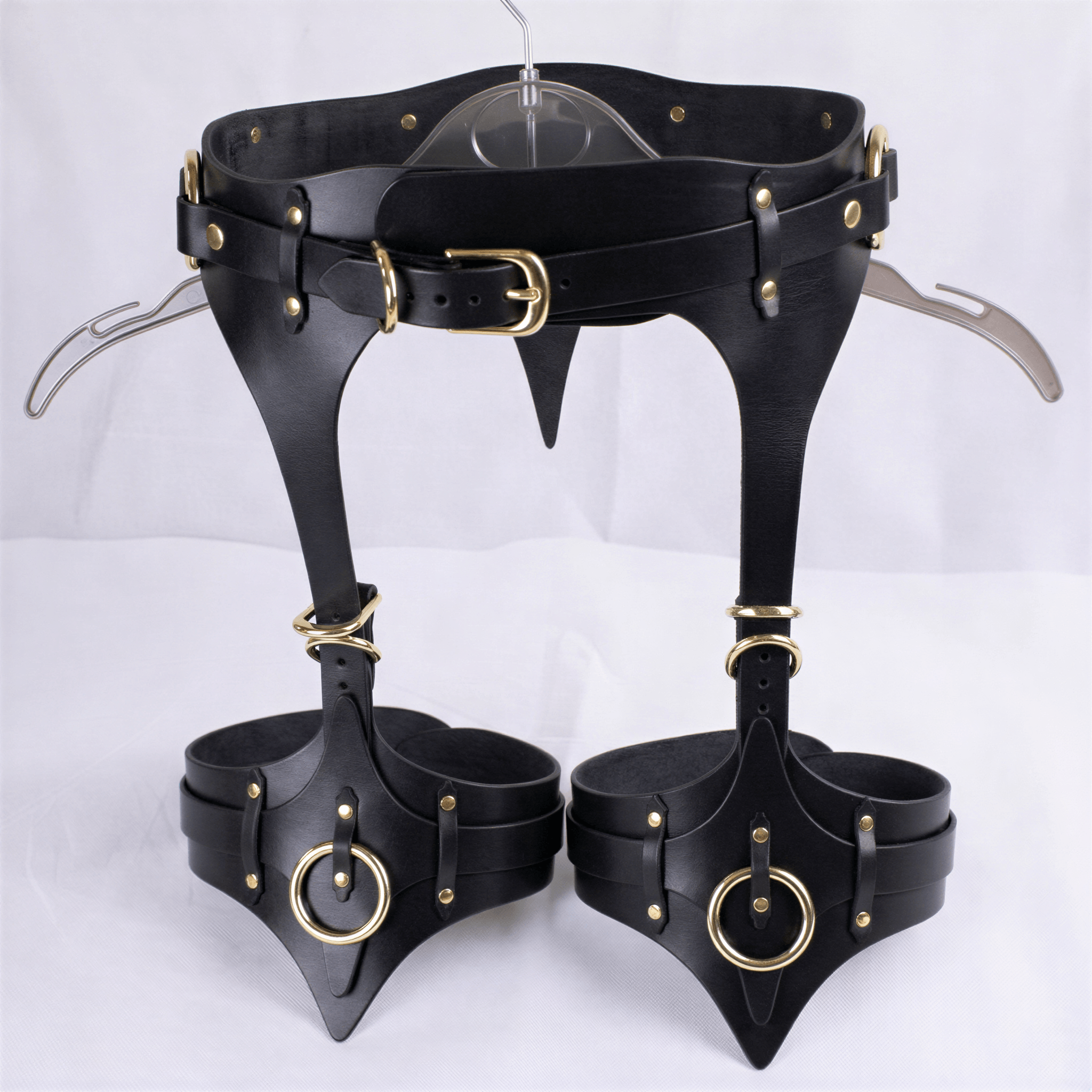 A pair of black leather garter belts with gold-colored buckles and rings, displayed on a white background.