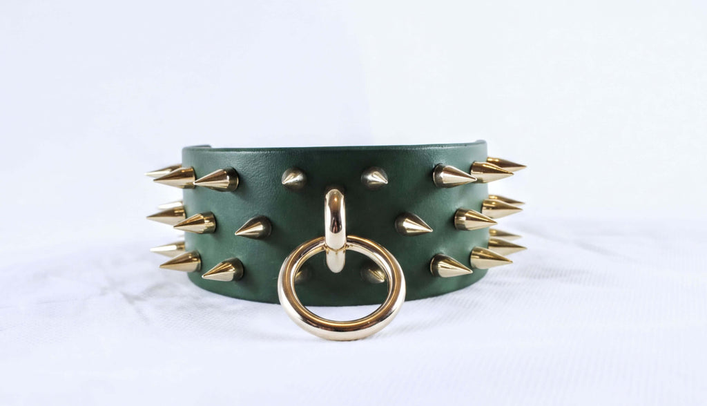 A green leather choker necklace with gold spikes protruding from it, and a gold ring with a circular hole in the center.