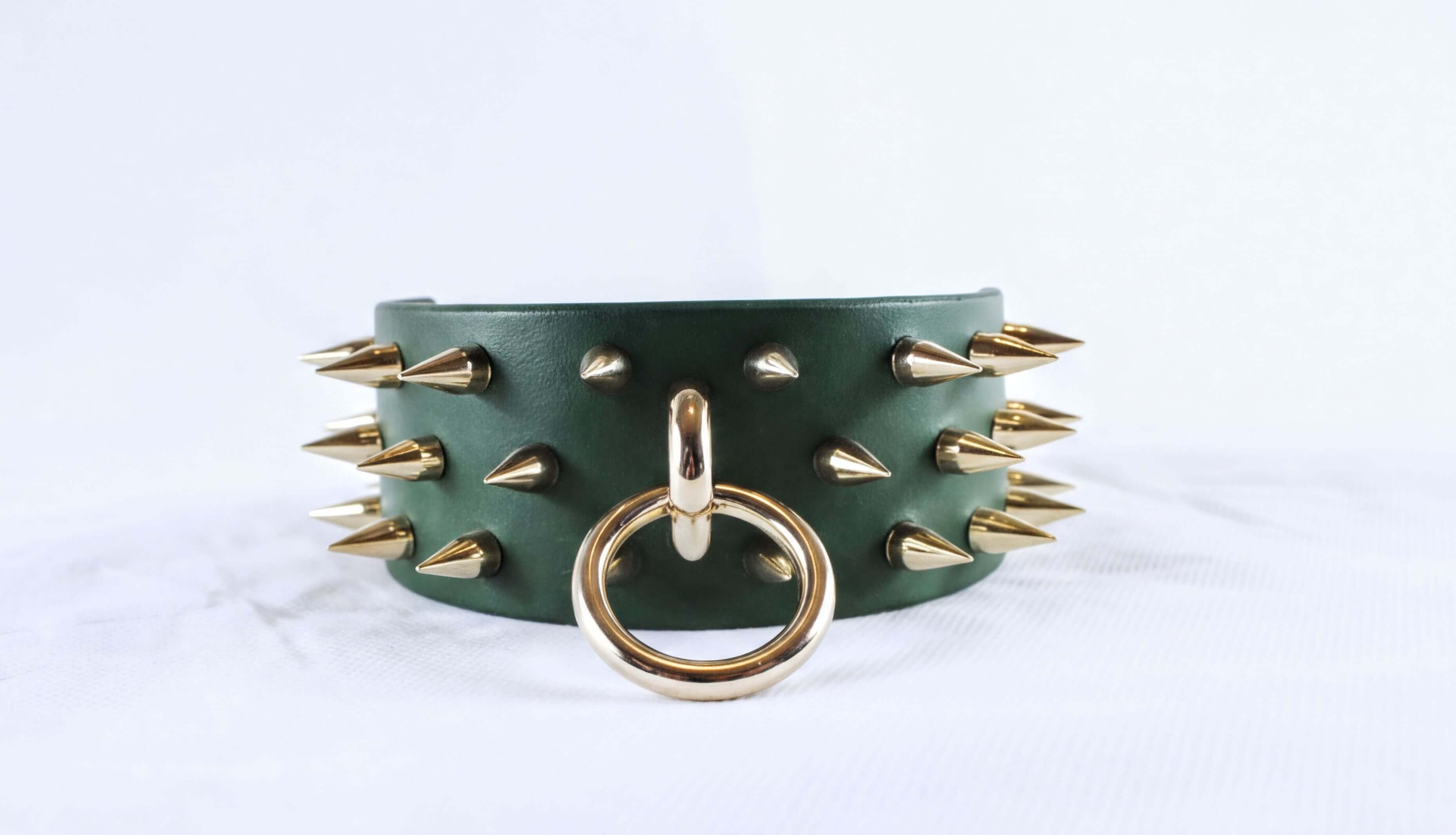 A green leather choker necklace with gold spikes protruding from it, and a gold ring with a circular hole in the center.