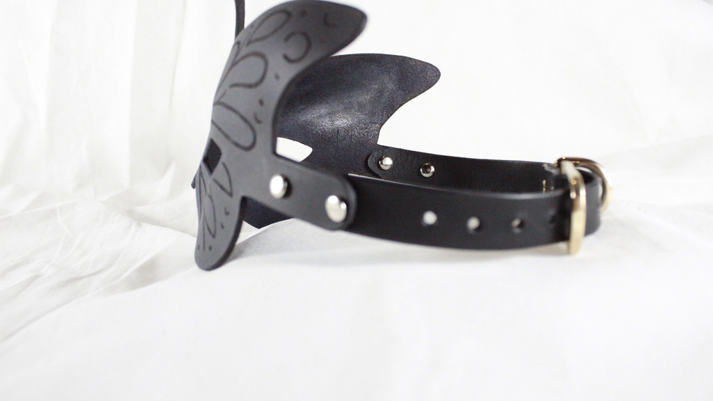 A black leather headband with a decorative butterfly design is shown against a white background.