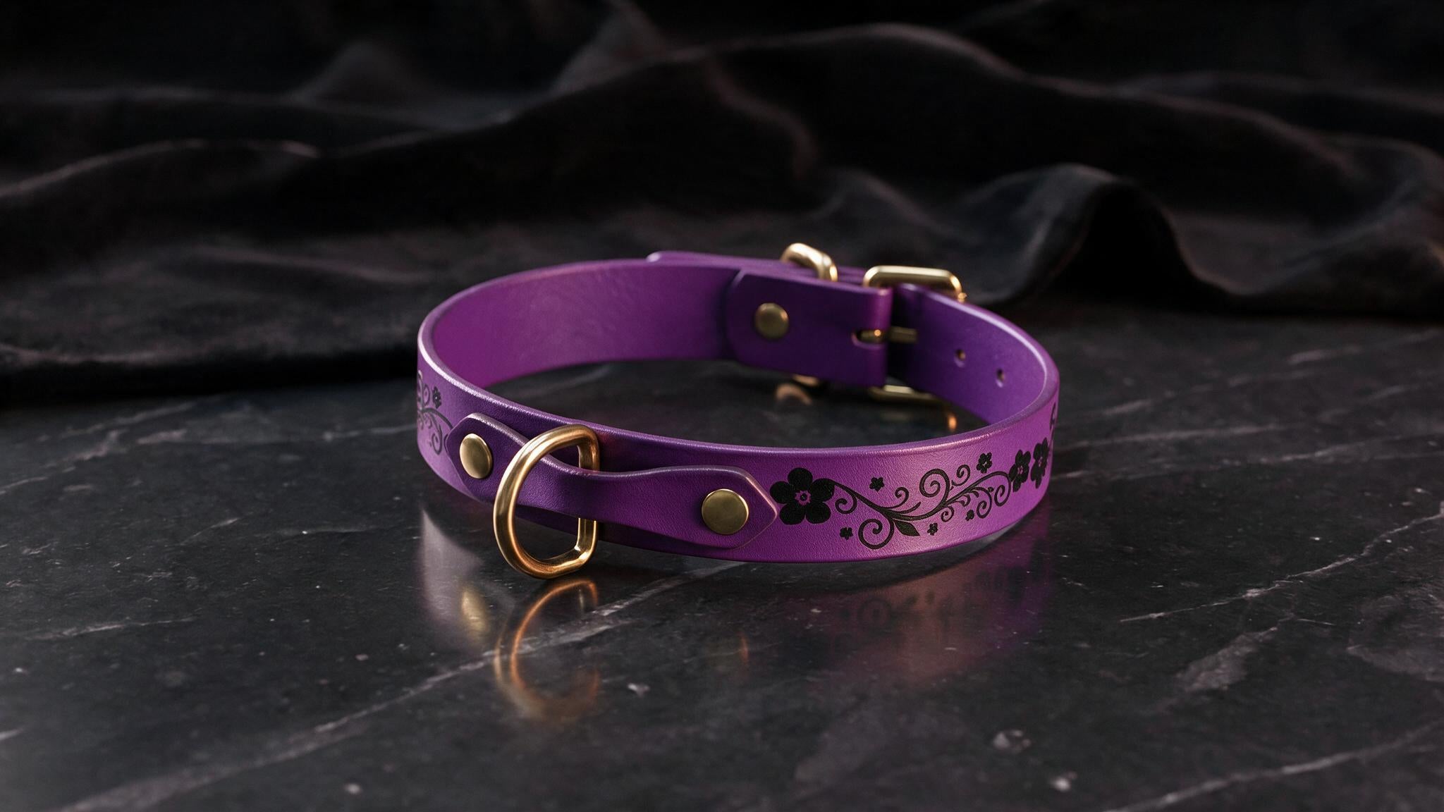 A purple leather collar with a floral design and gold hardware is displayed on a dark surface.