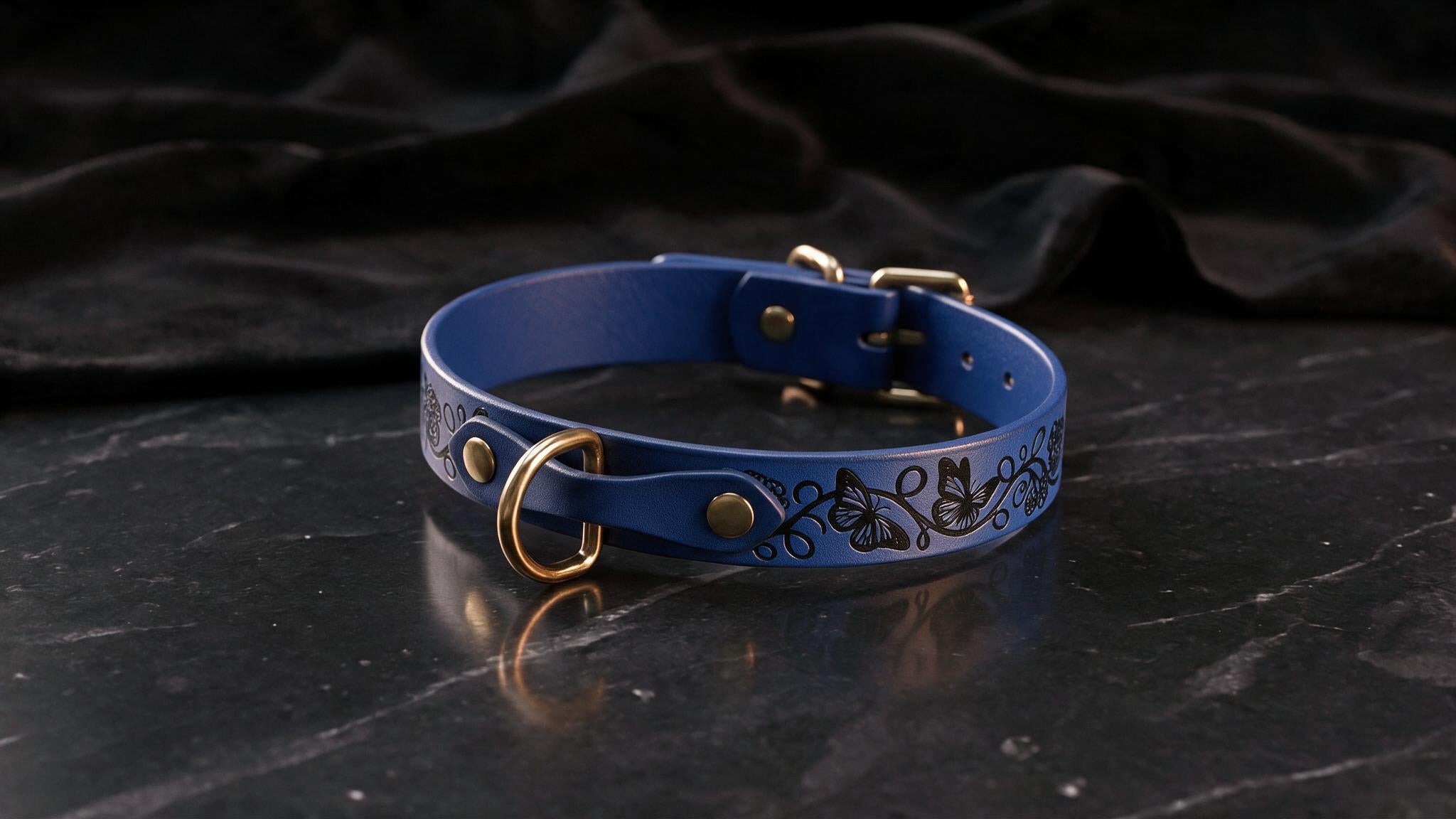A blue leather collar with a floral design and gold hardware is displayed on a black marble surface.