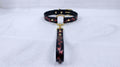 A black leather collar with a gold-colored metal ring and a red floral pattern on the strap.