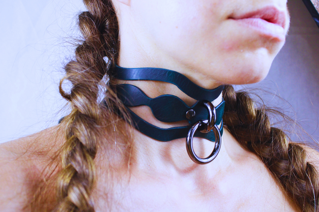 A close-up of a person's neck and chin wearing a dark blue choker necklace with a metal ring.