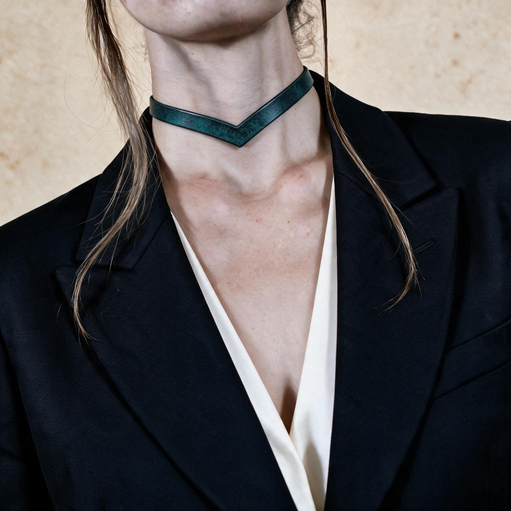 A close-up of a person wearing a black blazer and a green choker necklace.