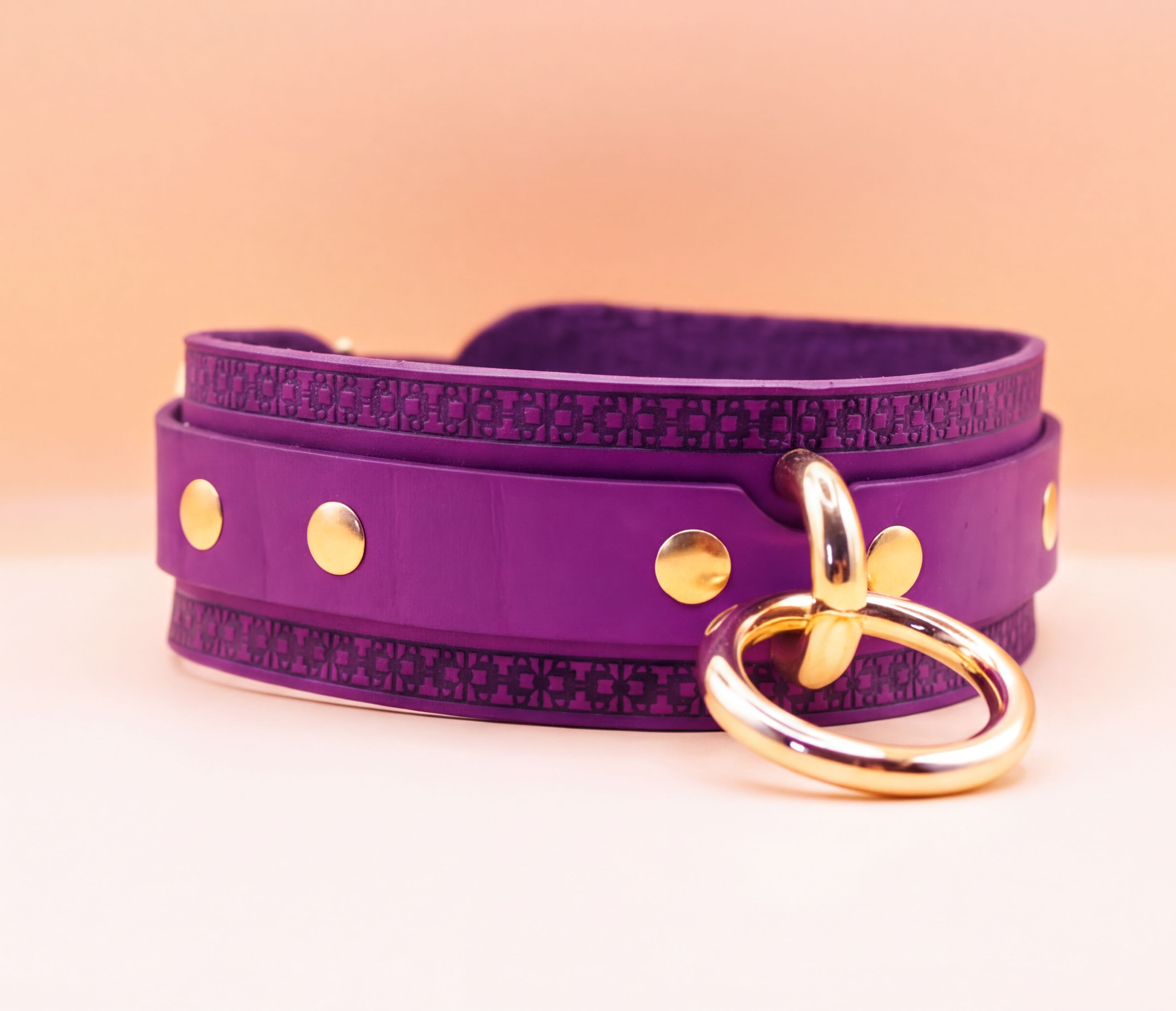 A purple leather choker necklace with a gold ring and three gold studs on the front.
