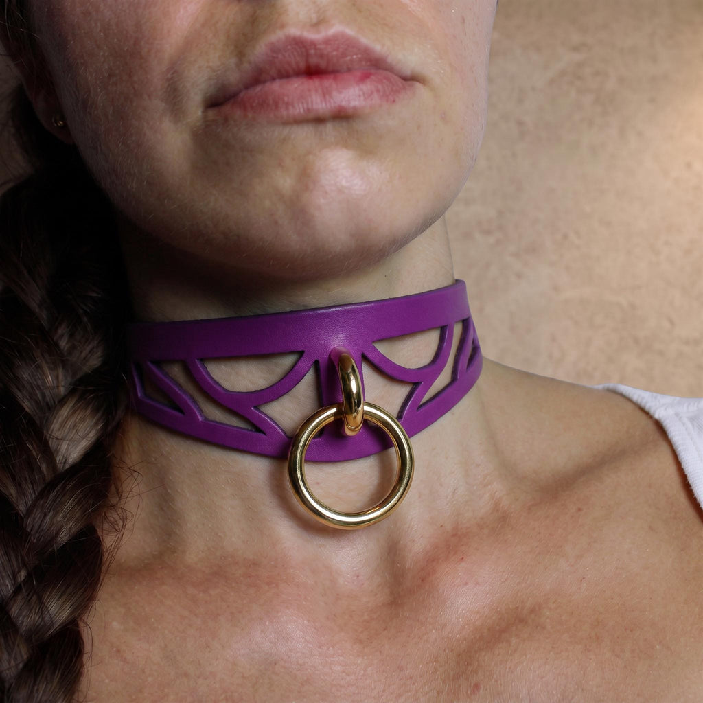 A close-up of a woman's neck and chest area, featuring a purple choker necklace with a gold ring and a gold ring on the collar.