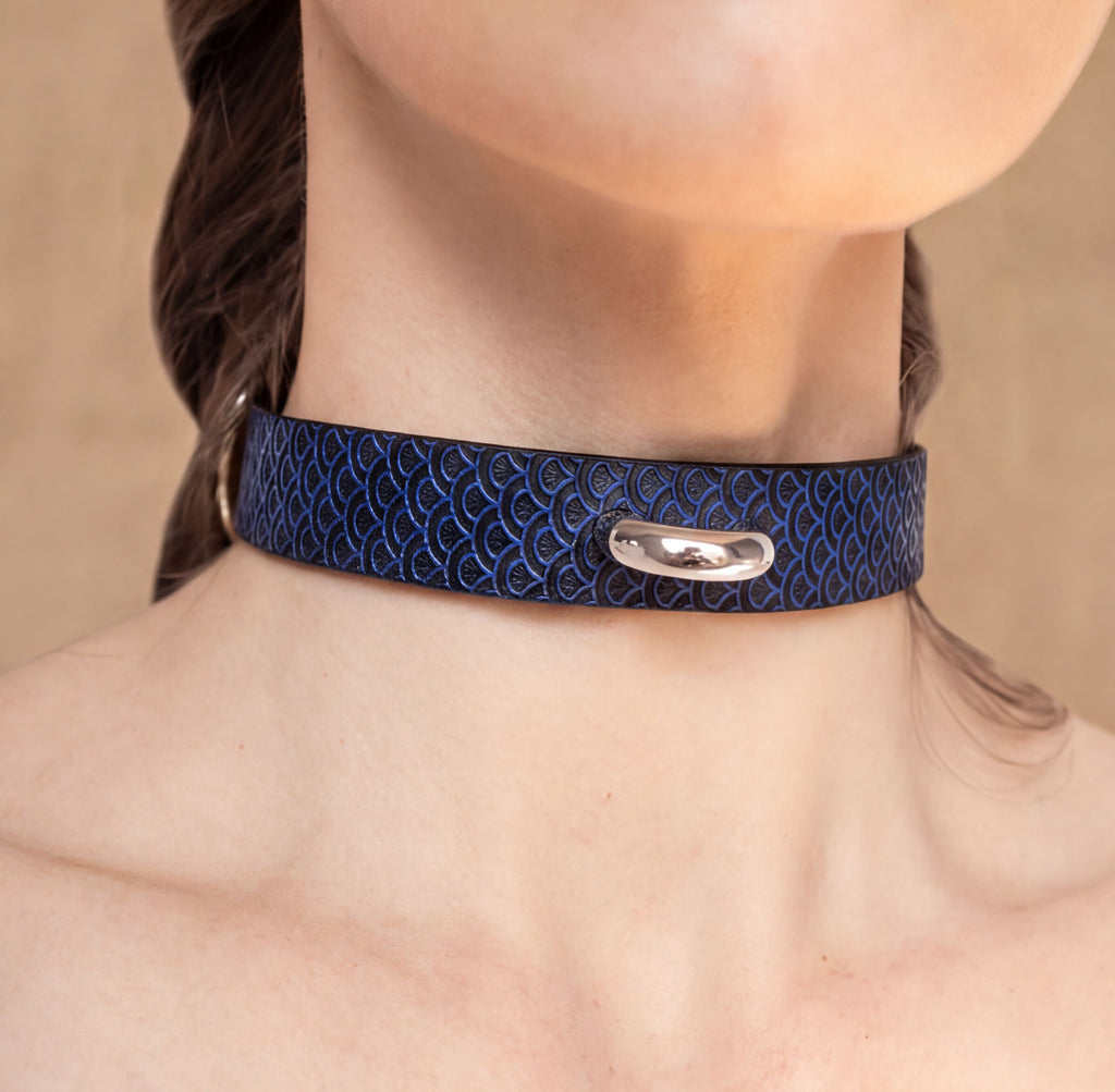 A close-up view of a person's neck and chest area wearing a blue patterned choker necklace with a silver clasp.