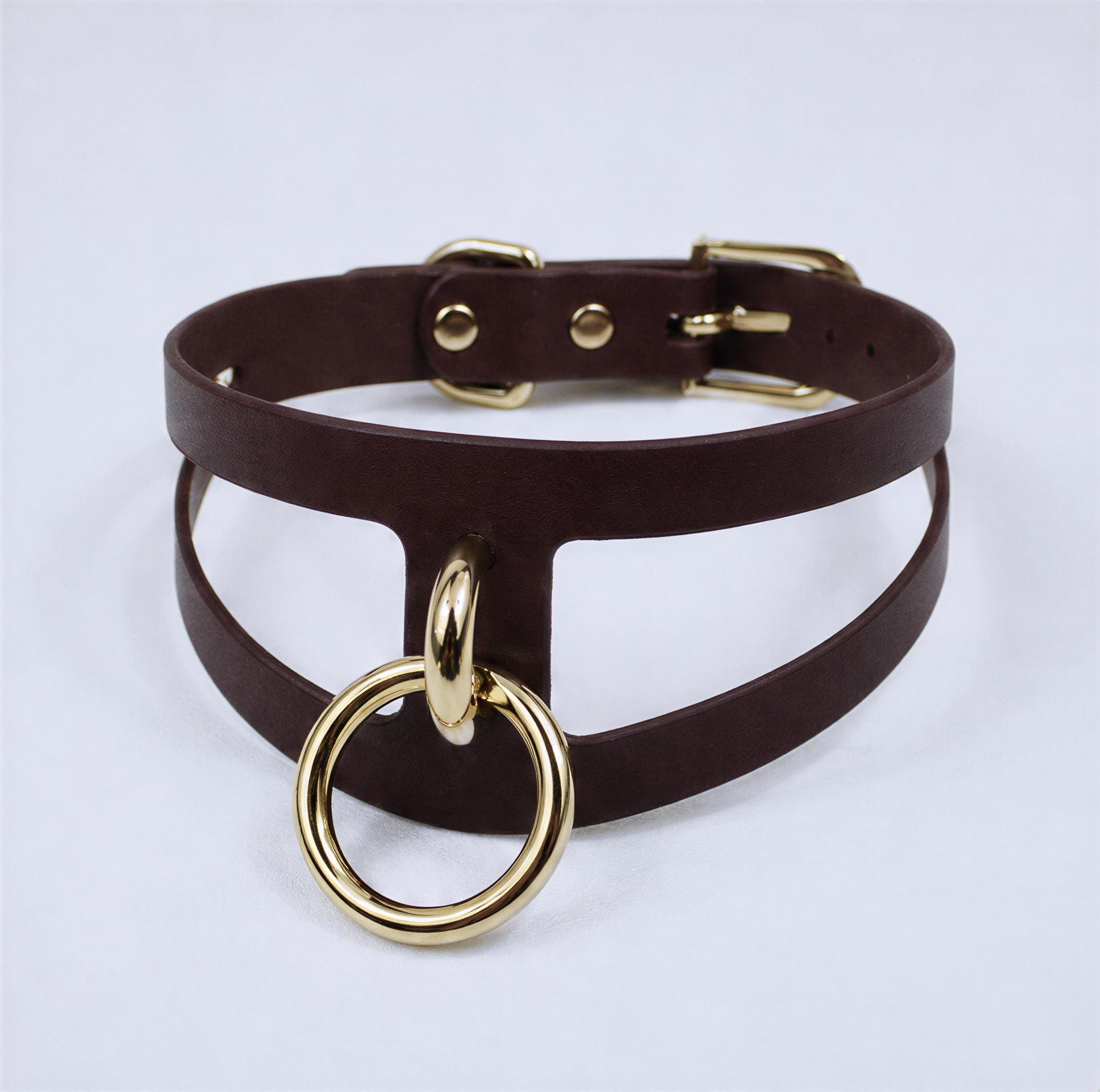 A dark brown leather choker necklace with a gold-colored metal ring and buckle.