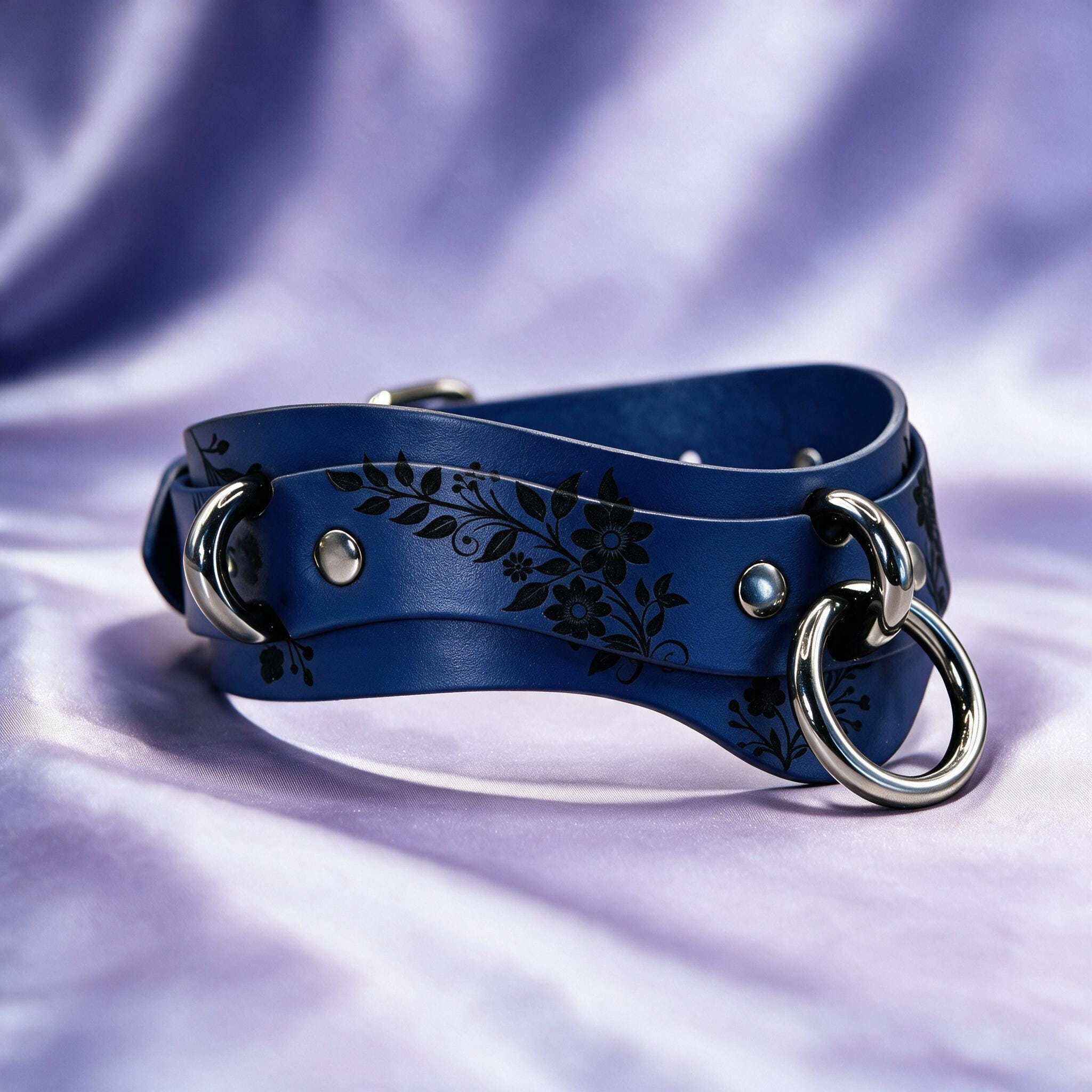 A blue leather strap with a floral design and metal rings on it, resting on a purple background.